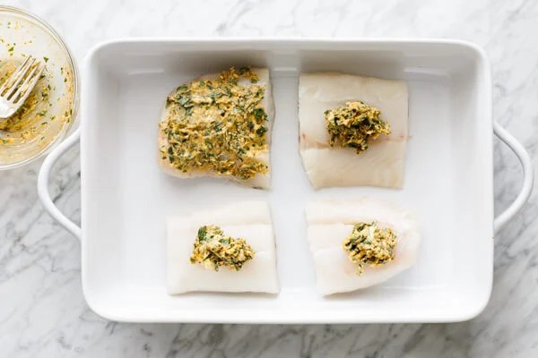 Garlic butter being spread on top of cod filets.