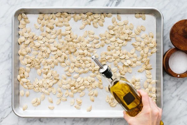 Drizzling oil for roasted pumpkin seeds on a baking sheet.