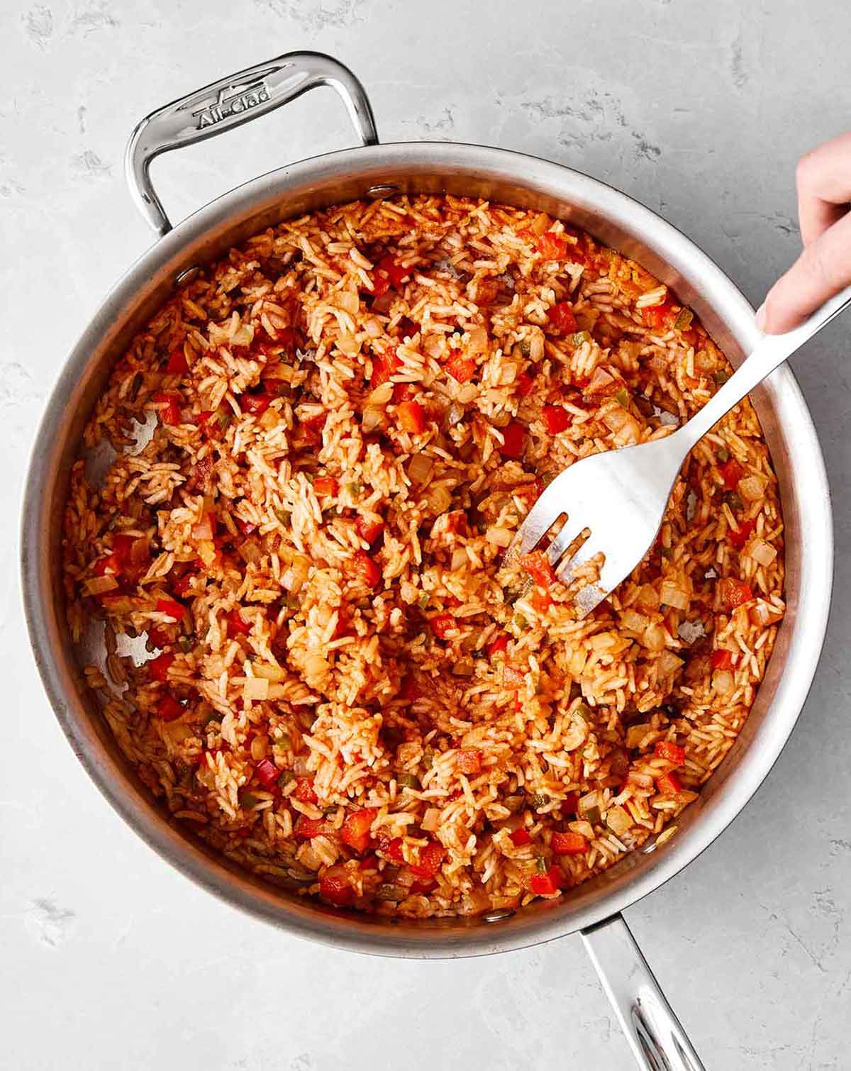 This Mexican rice is the perfect side dish for your dinner spread! It's layered with authentic flavor, really easy to make, and loved by all. Fluffing Mexican rice in the pan before serving.