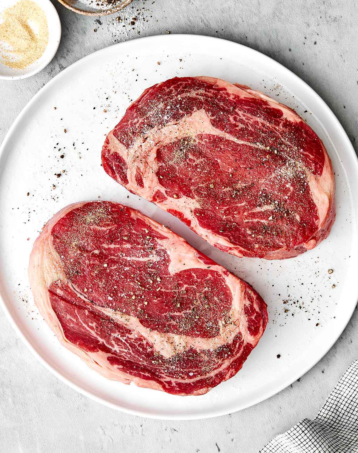 After testing different grill temperatures and timing, this is the grilled ribeye steak recipe I always come back to for a juicy medium-rare! Seasoning ribeye steaks on a plate.