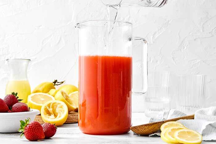 Mixing strawberry lemonade in a pitcher.
