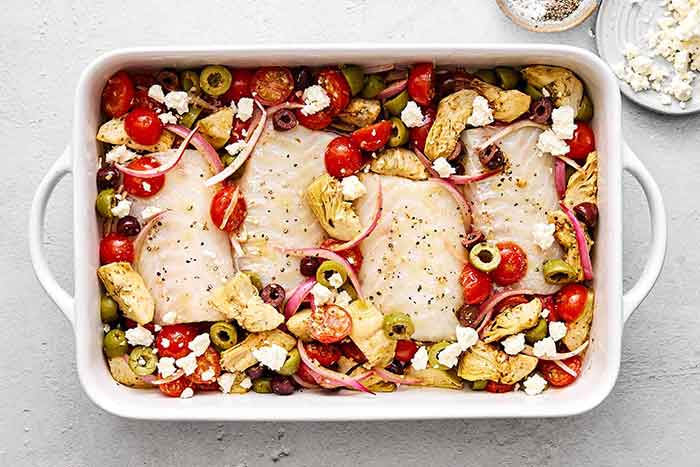 Cod nestled with veggies in casserole dish.