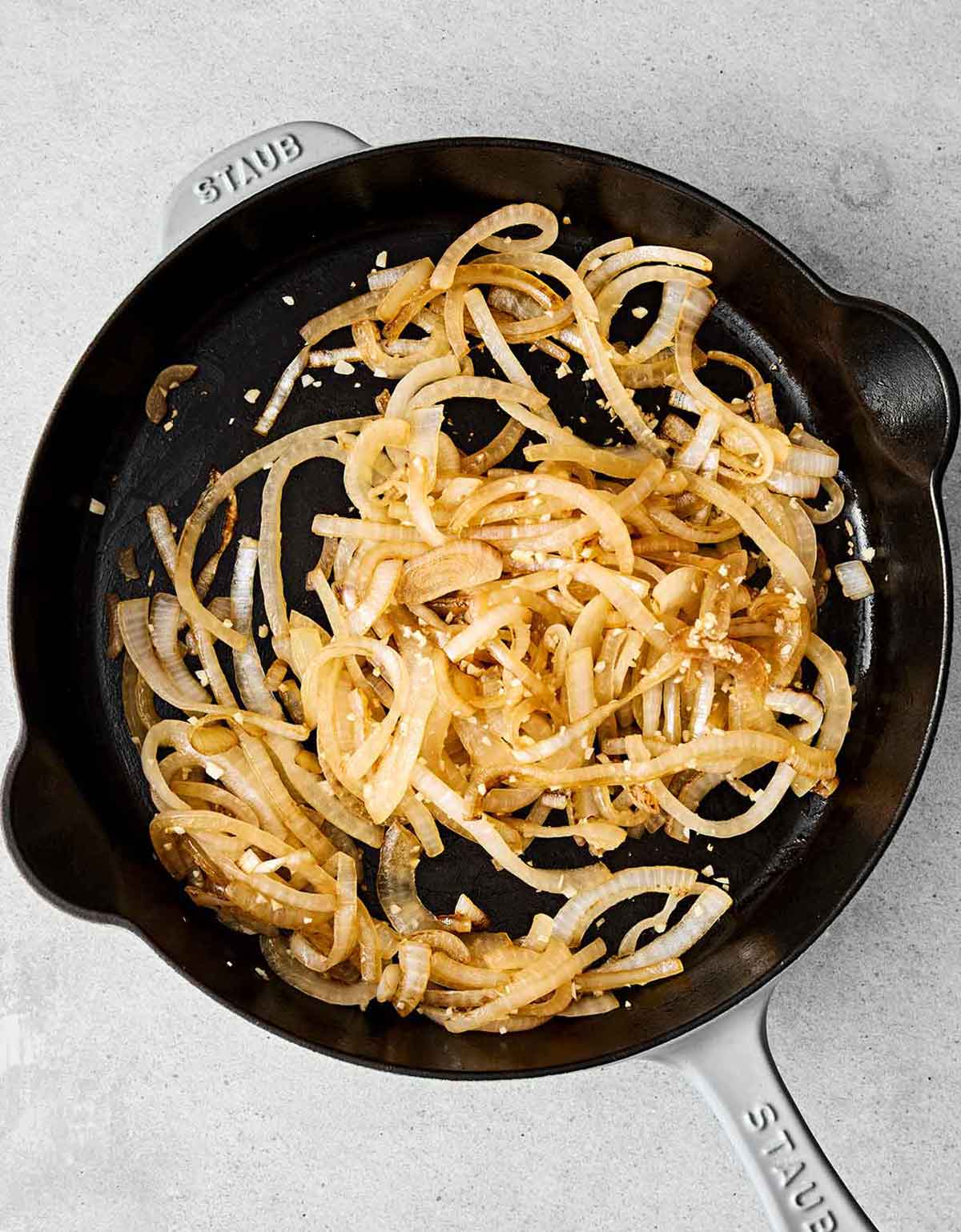 You'll eat this Mexican chicken tinga on repeat! It's made with shredded chicken, a smoky tomato-chipotle sauce, and caramelized onions. Sauteed onions in a pan for chicken tinga.