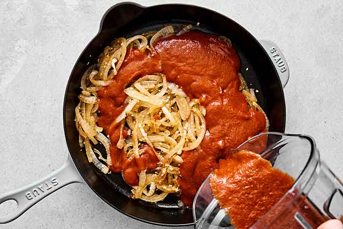 Mixing chicken tinga sauce with onions in a pan.