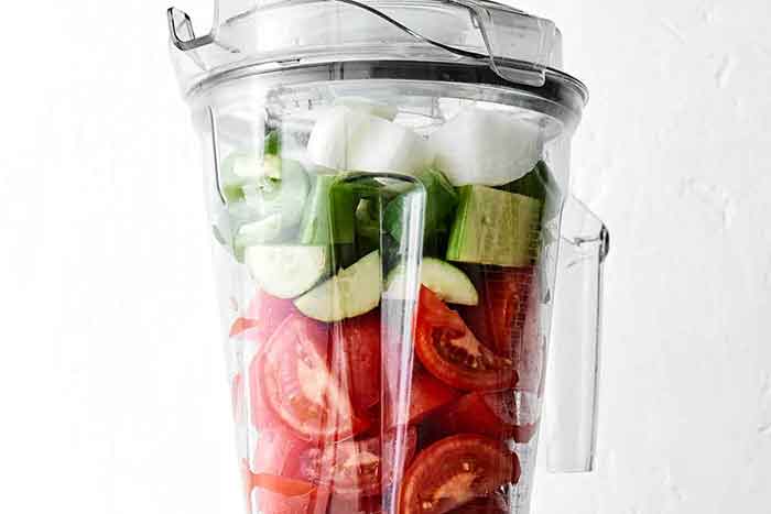 Adding gazpacho ingredients to a blender.