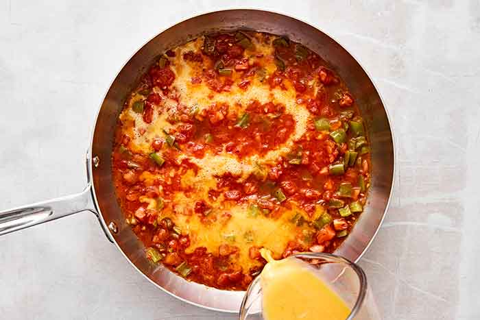 Adding scrambled eggs to a menemen dish.