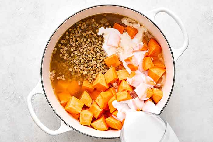 Adding sweet potatoes and lentils to a soup.