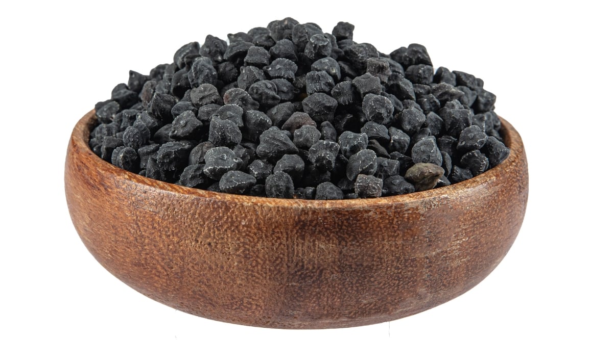 Dark hard black beans sitting in a wooden bowl against a white background. The legumes appear dry, and are not yet cooked.