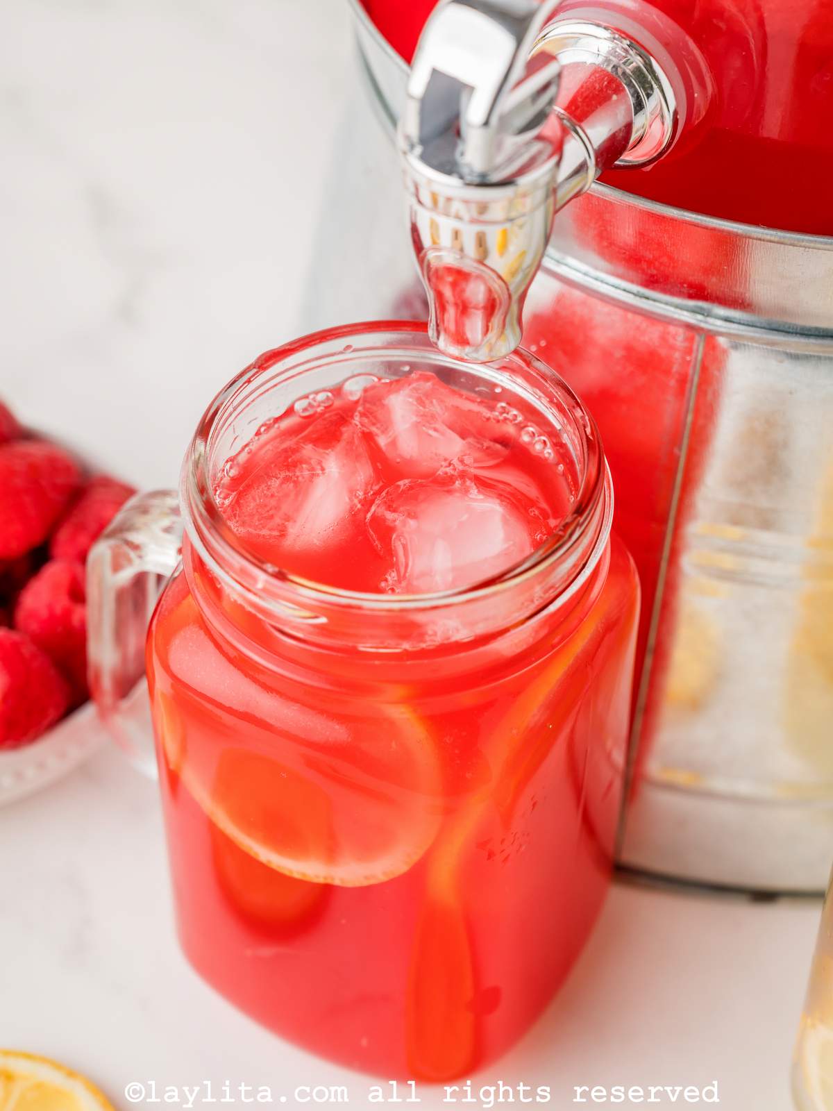 A masor jar glass being filled with raspberry lemonade from a dispenser