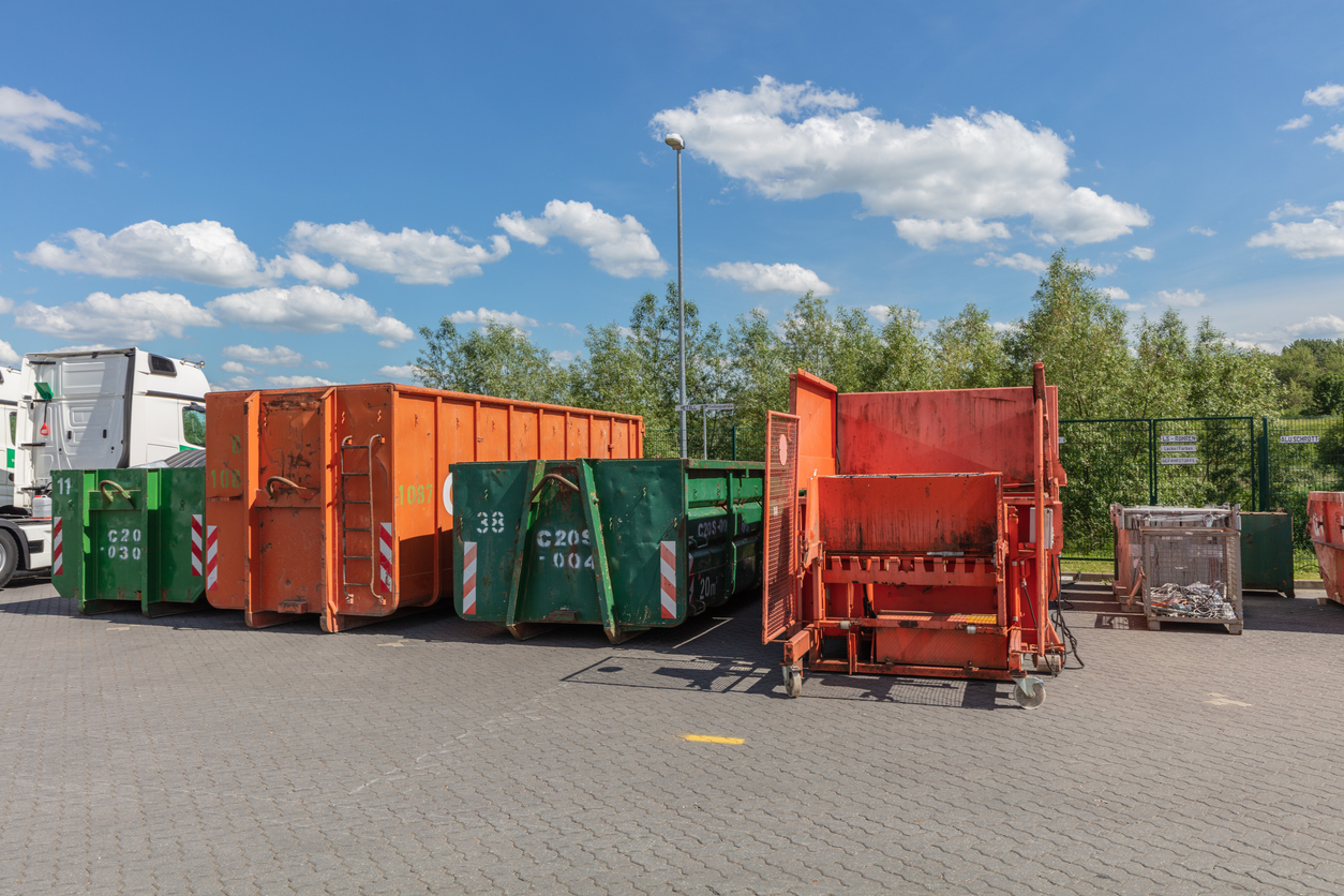 orange waste compactors are standing on a factory site with other waste