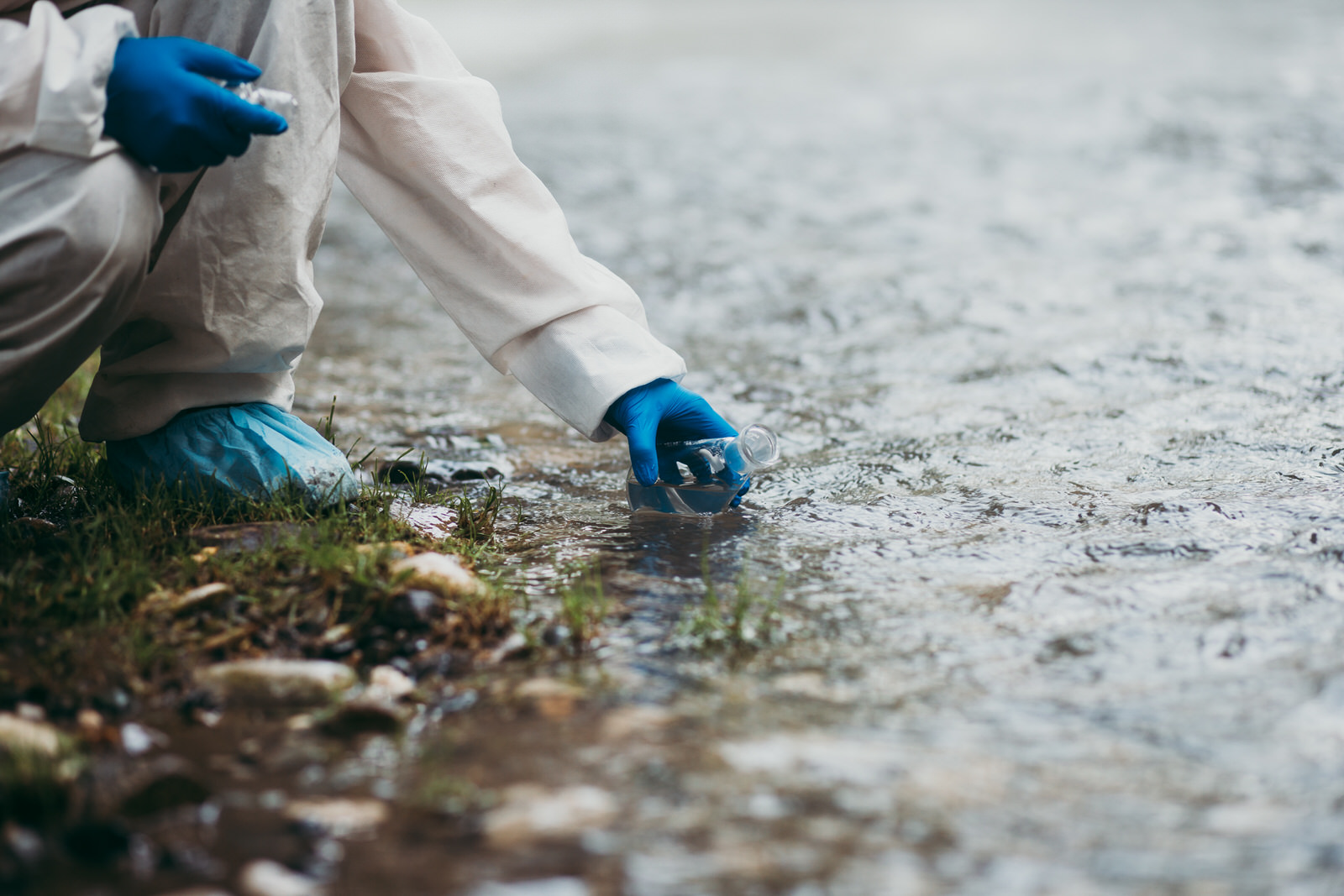 Scientist in protective suite taking water samples from the river