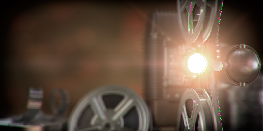Movie projector with light beam and film reels on dark backgroun