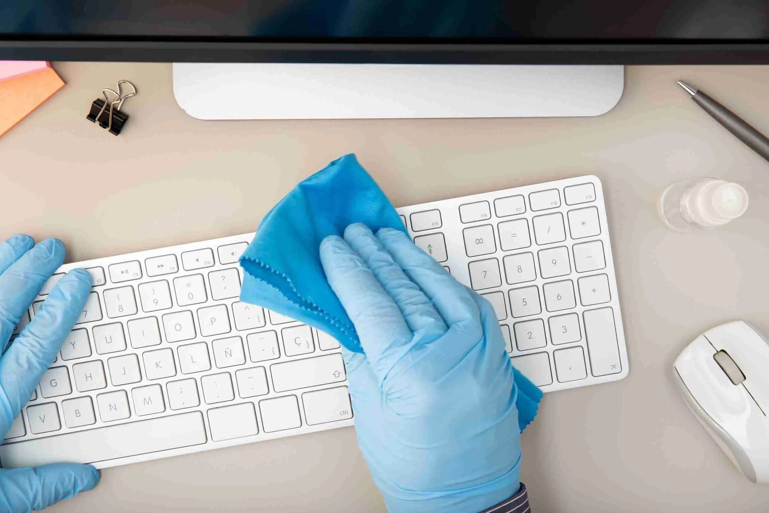 Hand with protective glove cleaning a keyboard with disinfectant