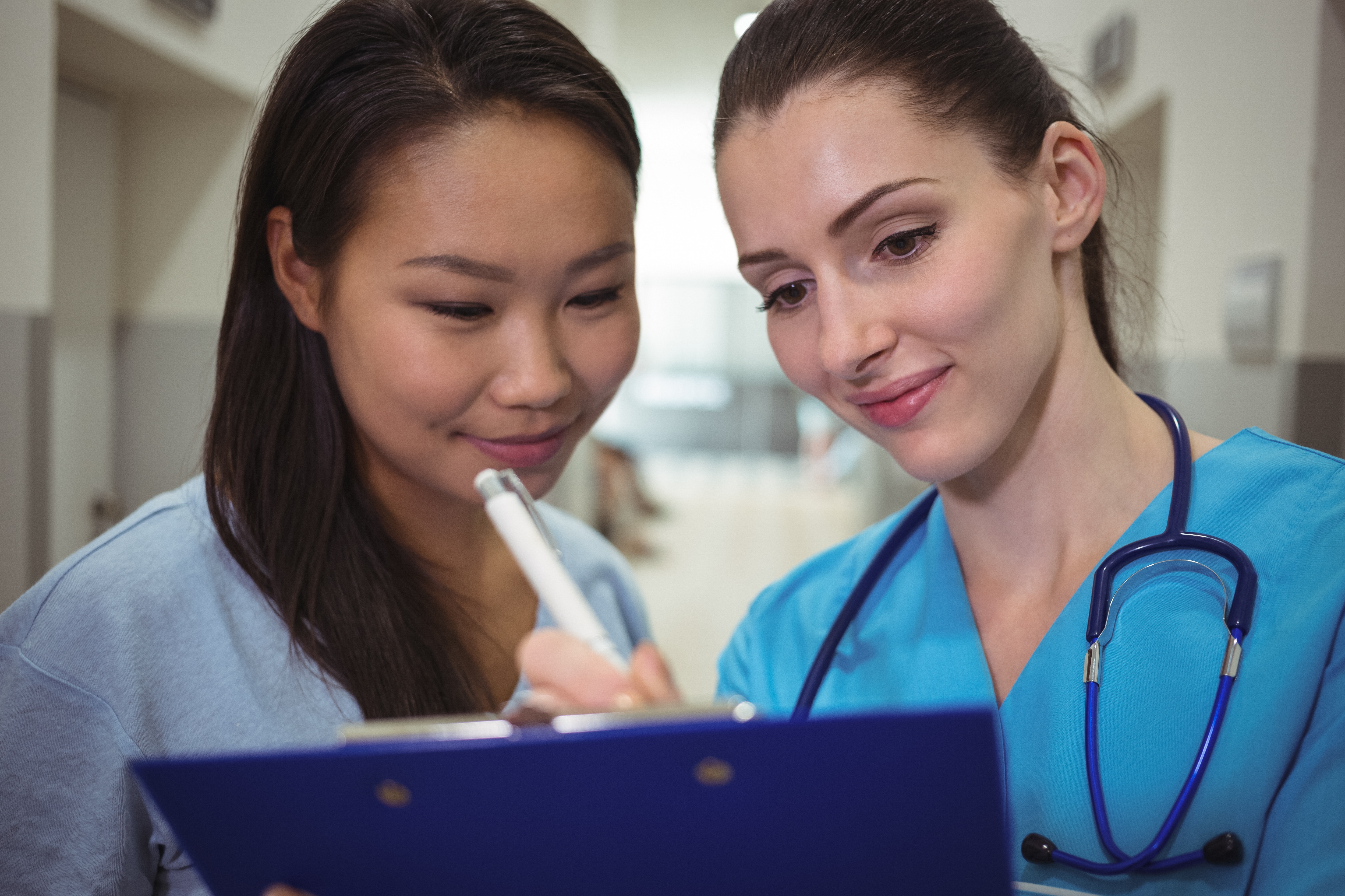 Female nurse assisting patient on clipboard Scrubs Academy