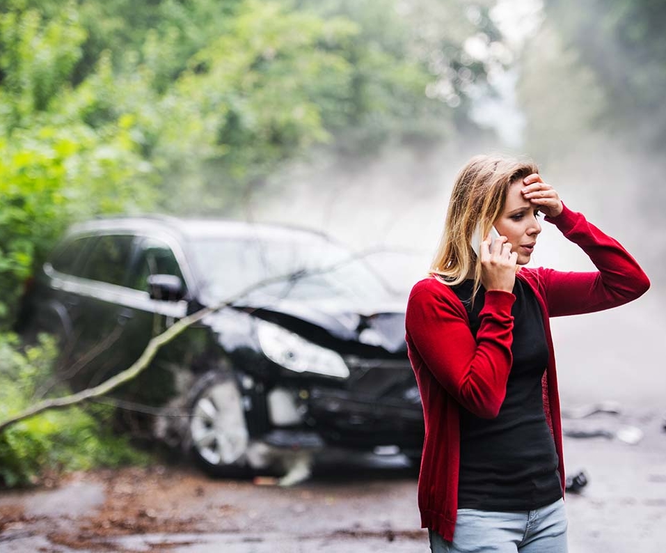 A young woman with smartphone by the damaged car after a car accident