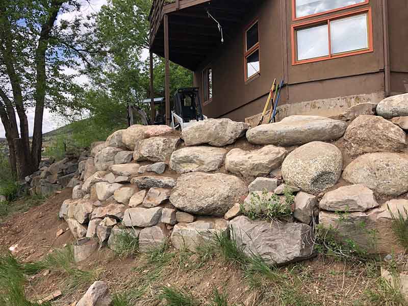 Boulder retaining wall with red flagstone yard treatment in Lyons