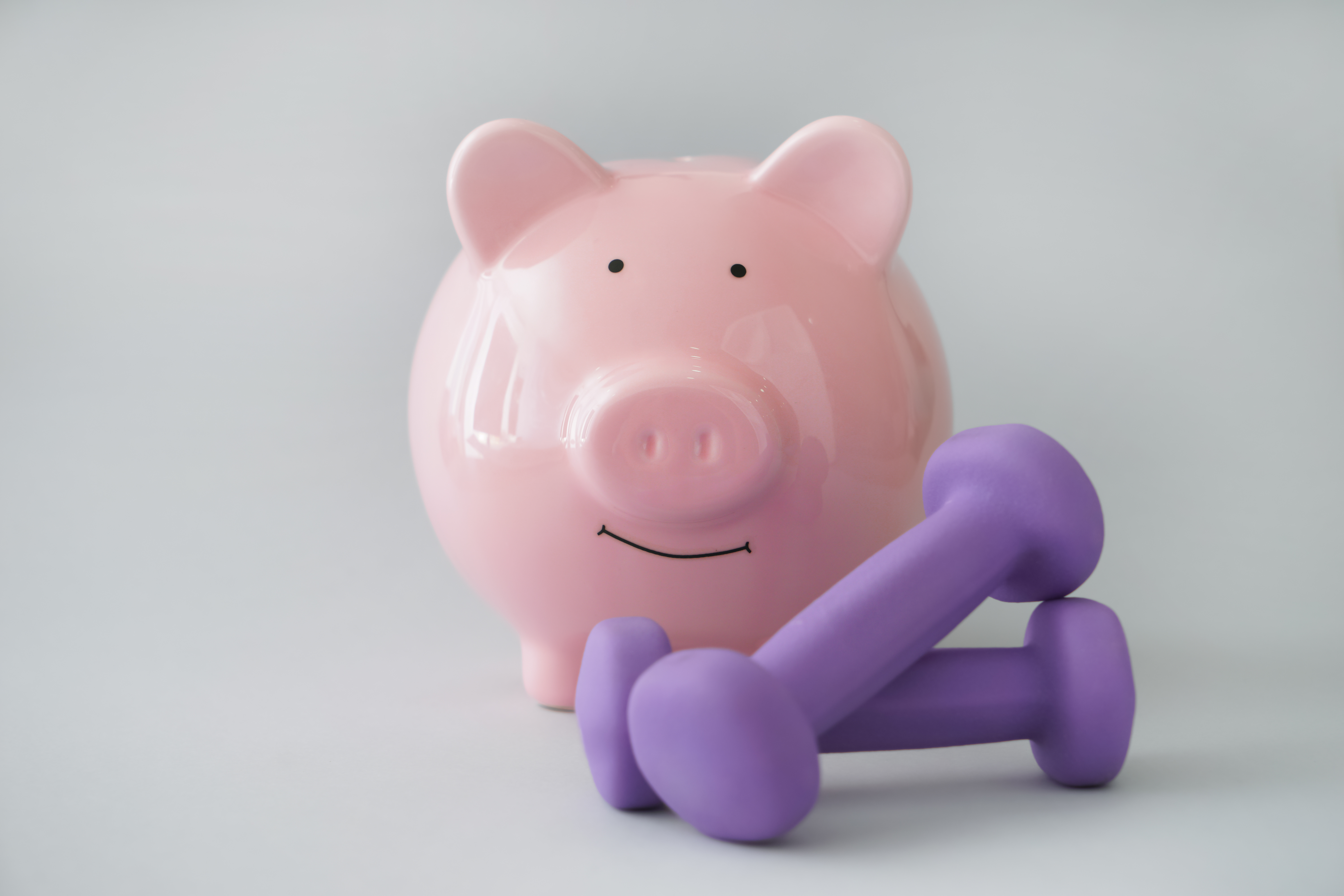 Piggy bank with dumbbells on light background. Weight loss concept