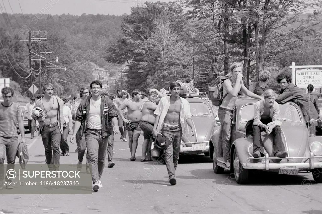 1960s AUGUST 1969 TEENS WALKING AND ON VW BEETLES CARS ON THEIR WAY TO