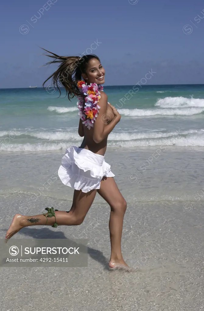 Young woman running on a sunny beach wearing a white skirt and leis