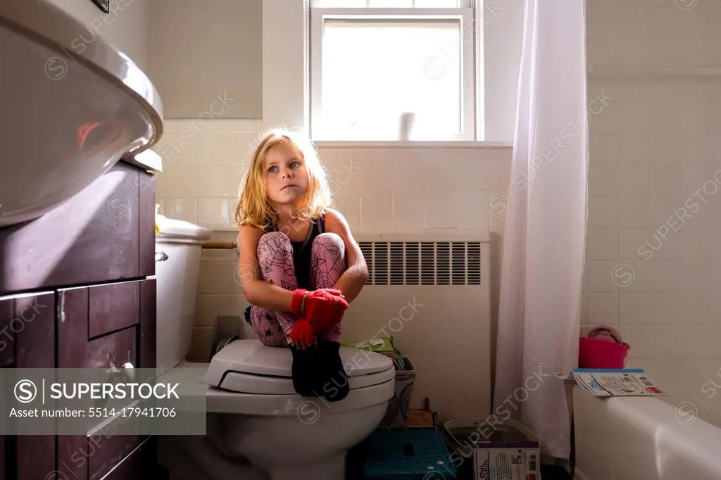 little girl sitting on toilet looking off to the side with somber look