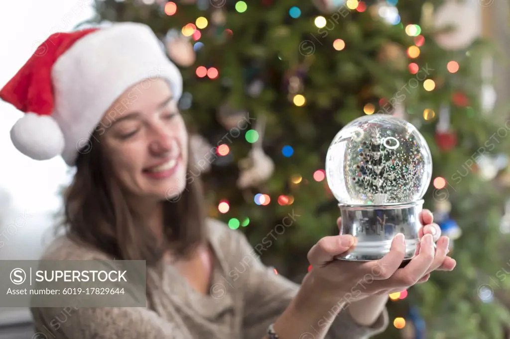 Collegeaged woman looking at Christmas snowglobe by Christmas Tree SuperStock