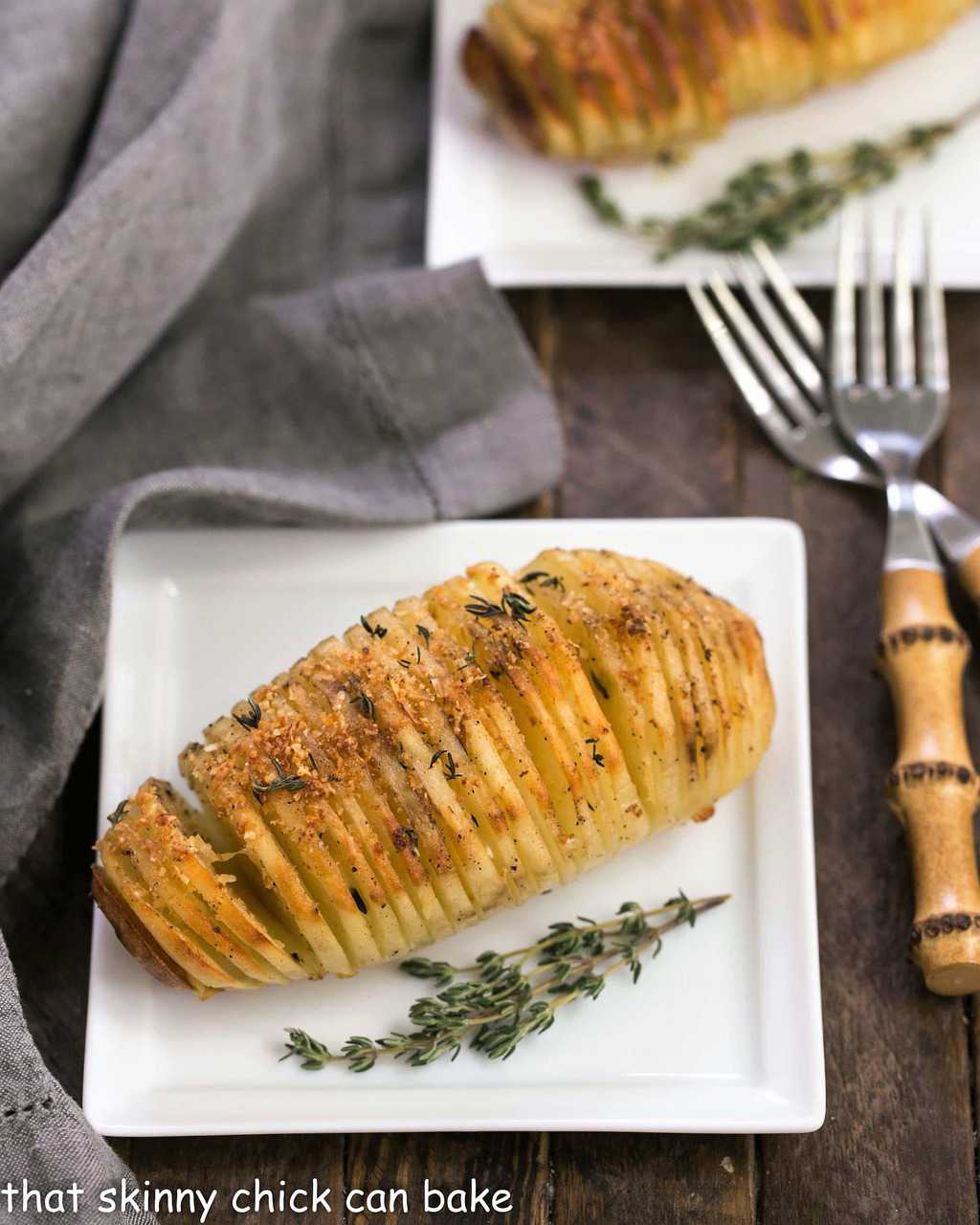 Hasselback Potatoes - Seasoned Fanned Potatoes that will delight your palate! Fanned Potatoes on square white ceramic plates with bamboo forks.