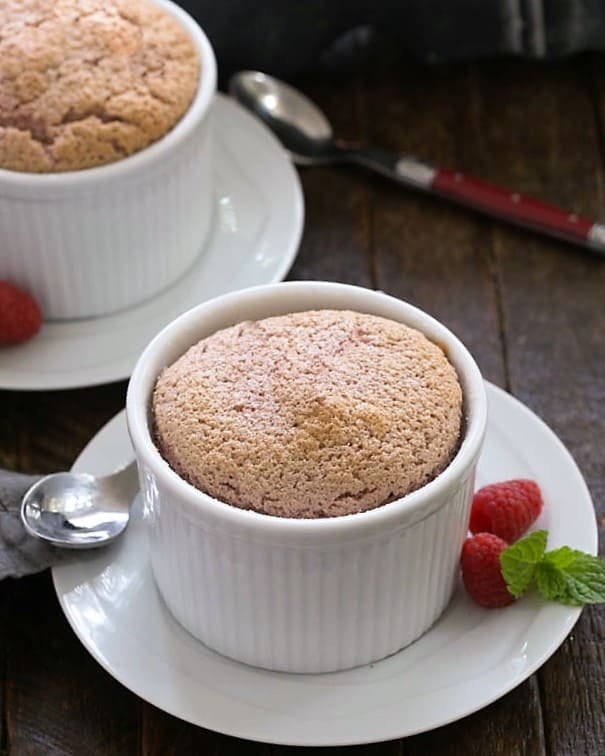 Individual Raspberry Souffles - an elegant dessert recipe you can make at home! This restaurant worthy berry dessert will wow your guests. Two raspberry souffles on white dishes with spoons.