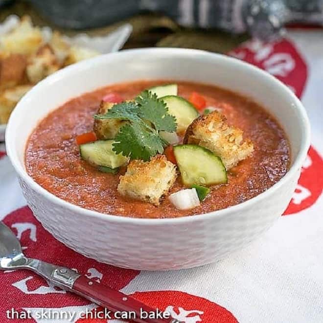 Gazpacho Recipe with Homemade Croutons - A chilled Spanish tomato soup topped with diced vegetables and homemade croutons Classic Gazpacho with Homemade Croutons in a white ceramic bowl with a red handled spoon.