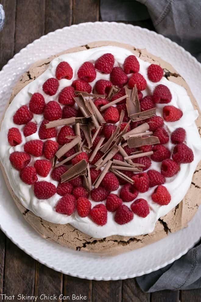 Chocolate Raspberry Pavlova - A sublime dessert with a chocolate meringue topped with berries and cream Overhead view of Chocolate Raspberry Pavlova on a white ceramic plate.