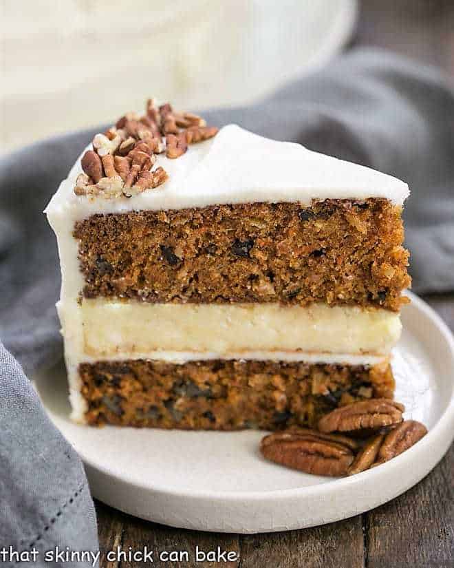 Cheesecake Filled Carrot Cake - Two decadent desserts in one for one showstopper of a cake! Slice of Cheesecake Filled Carrot Cake on a rimmed white plate with pecans.