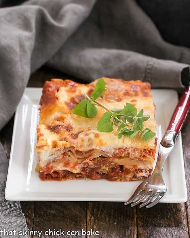 Ricotta Lasagna with Sausage - Layers of flavor from the slow cooked tomato, Italian sausage and loads of gooey cheese make this the best lasagna you'll ever taste! Lasagna with Italian Sausage on a white plate with a red handled fork.