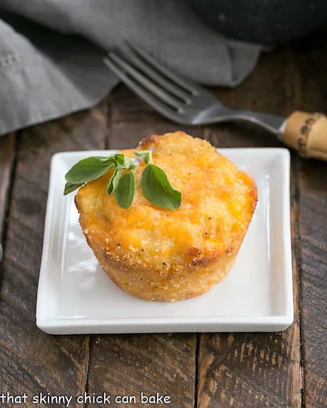 Individual Cheesy Potato Bake - a delicious cheese potato recipe the whole family will love Cheesy Potato Cup on a square white plate with a sprig of herbs to garnish.