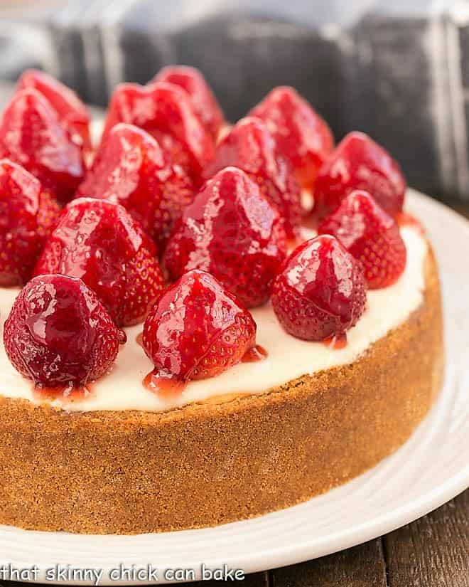 Strawberry Topped Cheesecake - a luscious, creamy vanilla cheesecake encased in a graham cracker crust with a sour cream topping and a crown of beautiful ripe, glazed strawberries! Strawberry Topped Cheesecake on white serving plate.