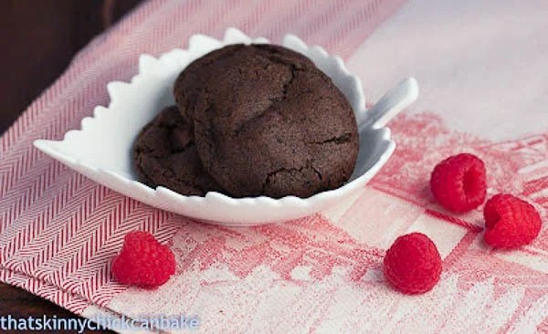 Chocolate cookies and cream cookies loaded with ground Oreos and cocoa powder for a magnificent chocolate fix! A close up of cookies and cream cookies in a white leaf bowl with raspberries surrounding it