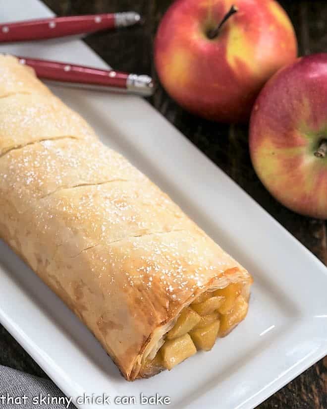 Apple Strudel with Phyllo is flaky, delicious and filled with sweet, cinnamon-spiced apples Apple Strudel dusted with powdered sugar on a white platter