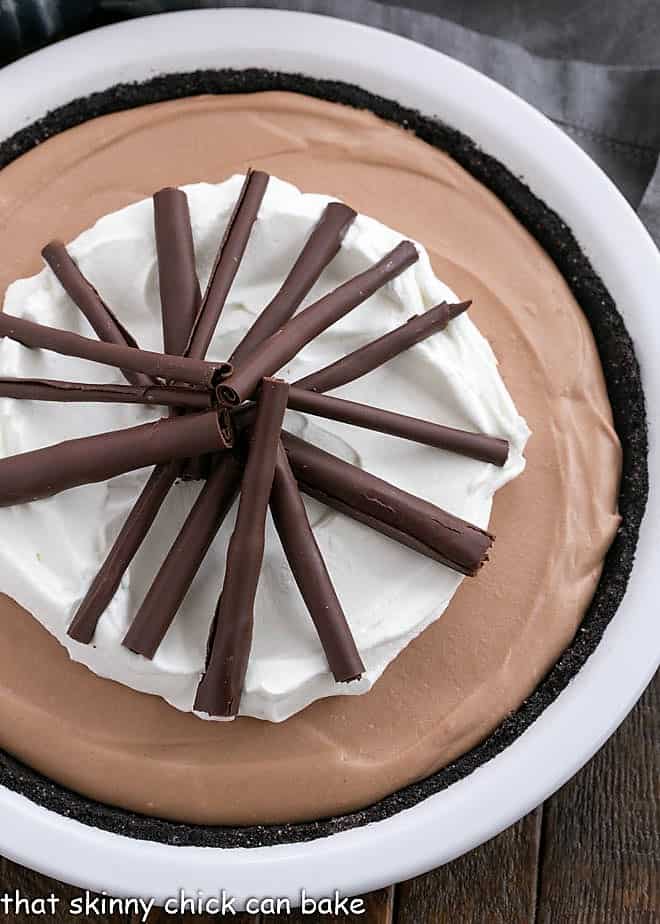 Chocolate Candy Bar Pie requires no baking and will get rave reviews from all the chocholics you know! Overhead view of Candy Bar Pie garnished with chocolate and whipped cream in a white pie plate.