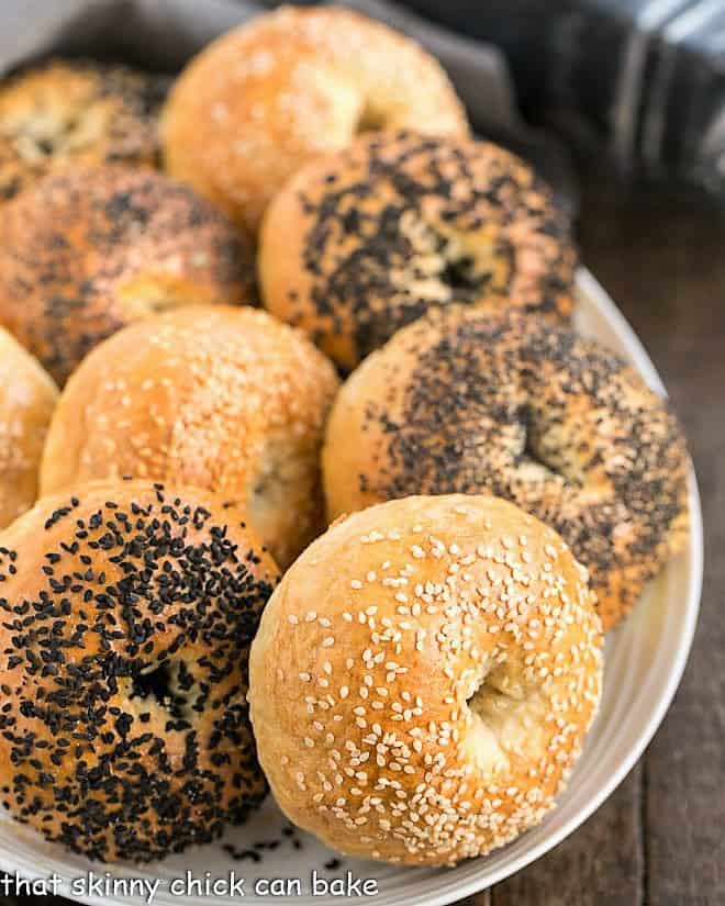 Dense, chewy Bagel Recipe sprinkled with seeds make for a marvelous breakfast or brunch treat. Making bagels from scratch will make you feel like an accomplished baker, plus your house will have a most enchanting aroma Homemade Bagels on a white oval tray.
