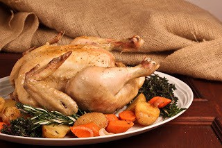 Wide view of Armagnac Chicken on a white platter with vegetables and herbs