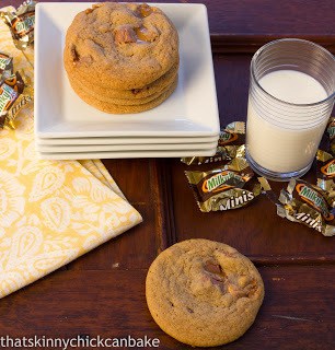 Milky Way Cookies are out of this world with a buttery, dark brown sugar base and chunks of candy bars!! These cookies are the perfect companion to a cold glass of milk. Milky Way Cookies on a stack of white serving plates next to Milky Way wrappers and a glass of milk.