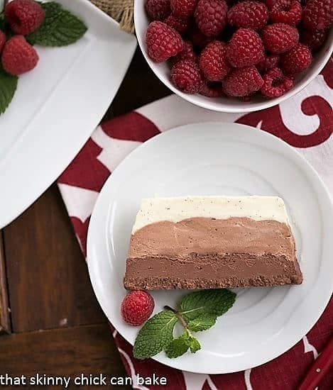 A 3 layer Chocolate Terrine - a no-bake triple chocolate mousse dessert! Triple Chocolate Terrine slice on a small white plate garnished with raspberries and mint.