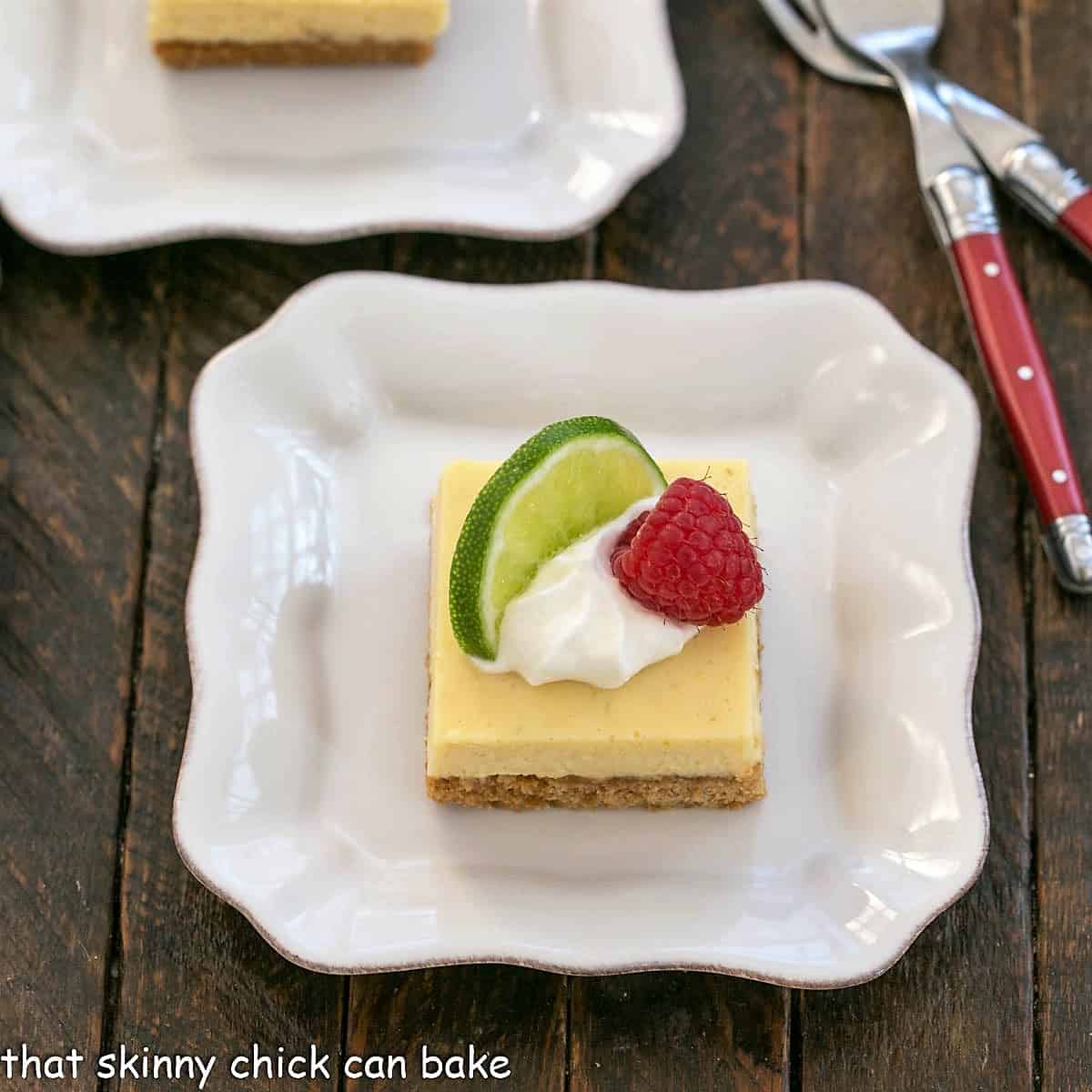 Key Lime Bars from my book club menu Overhead view of a key lime pie bar with a dollop of whipped cream, slice of lime and raspberry to garnish.