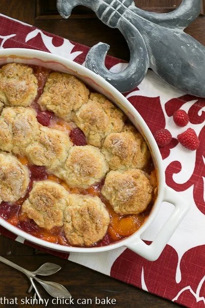 Peach Raspberry Cobbler - Sweetened fresh fruit dessert with a biscuit topping! Overhead view of a Fruit Cobbler in a white, oval casserole dish.