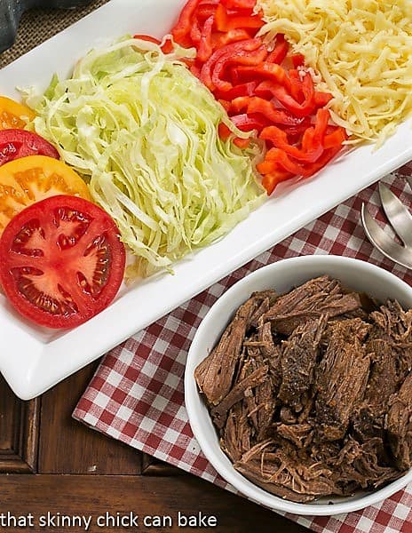 Slow Cooker Beef Barbacoa - Amazing barbecue beef in the slow cooker! Overhead view of Slow Cooker Beef Barbacoa in a white bowl with toppings on a white tray.