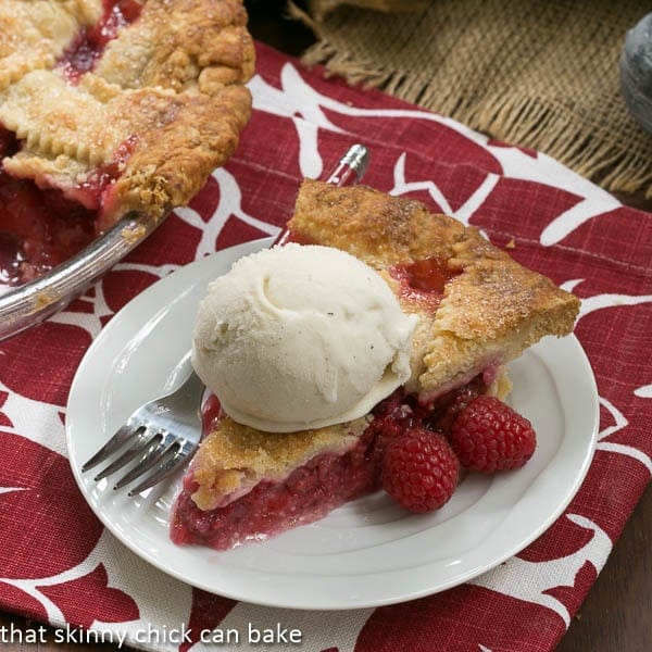 Lattice Topped Raspberry Pie on a white plate with a scoop of vanilla ice cream and a fork.