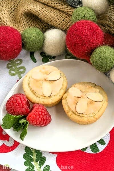 Raspberry Tarts Recipe - Raspberry jam and almond paste fill cream cheese pastry tartlets 2 Almond Raspberry Tartlets on an oval plate garnished with berries and mint.