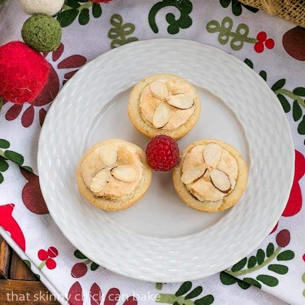 Raspberry Tarts - Raspberry jam and almond paste fill cream cheese pastry tartlets 3 Almond Raspberry Tartlets on a white plate with a raspberry garnish.
