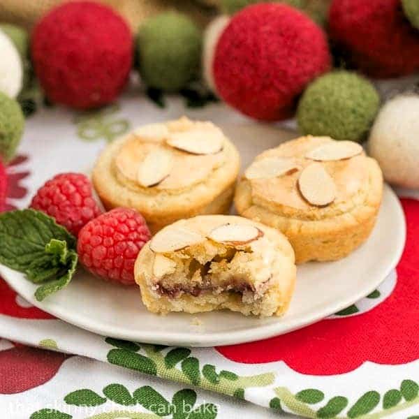 Almond Raspberry Tartlets -| Raspberry jam and almond paste fill cream cheese pastry tartlets Almond Raspberry Tartlets on a white plate with interior exposed on one tart.