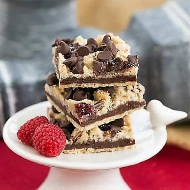Chocolate Raspberry Crumb Bars - Shortbread, fudge, jam and a layer of crumbs makes for an out of this world bar cookie! Chocolate Raspberry Crumb Bars on a small white pedestal.