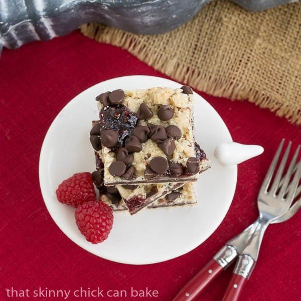 Chocolate Raspberry Crumb Bars - Shortbread, fudge, jam and a layer of crumbs makes for an out of this world bar cookie! Overhead Chocolate Raspberry Crumb Bars on a white pedestal on a red napkin.
