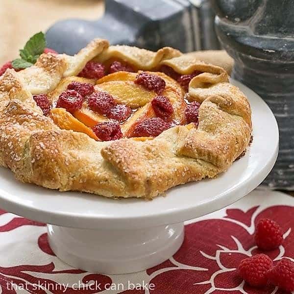 Peach Raspberry Galette - A rustic tart that's so much easier to make than pie! Peach Raspberry Galette on a white ceramic cake stand on a red and white napkin.